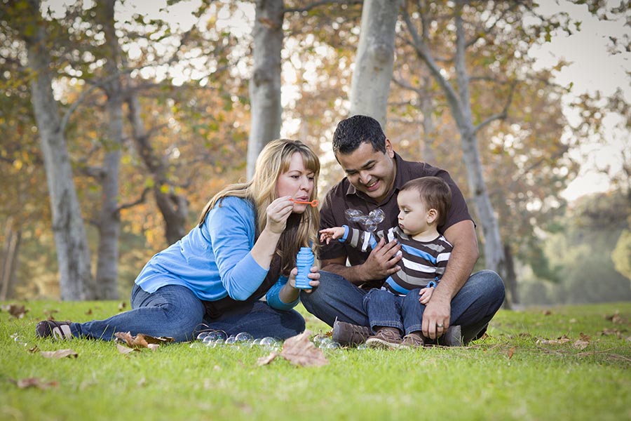 Contact Us - Family Sits With Baby in a Park Blowing Bubbles on a Sunny Autumn Day